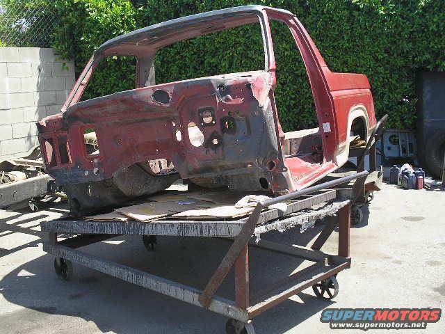 Red 1986 Ford Bronco body on a cart, showing interior and front quarter view