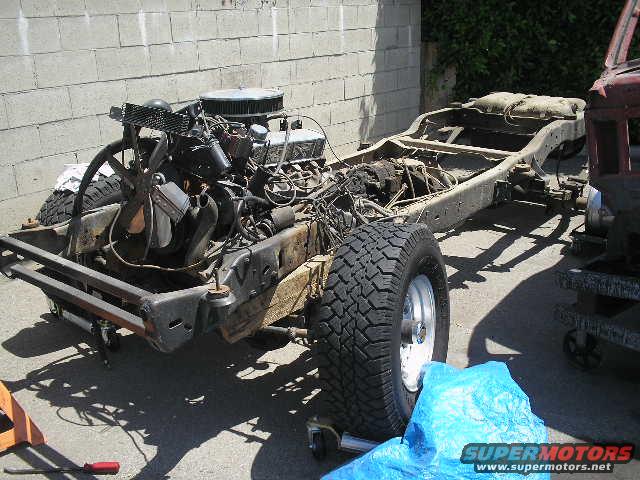 Vehicle frame and engine assembly on a sunny day, with a blue tarp in the foreground