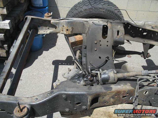 Rusty vehicle frame with suspension parts and a tire visible