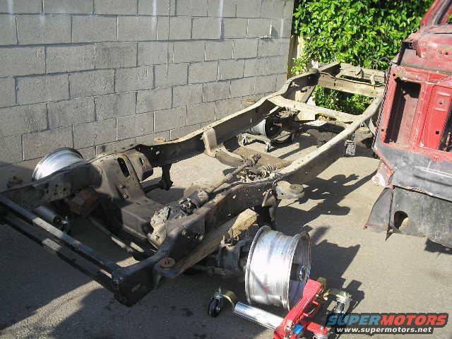 Vehicle frame and red body section on pavement, with a wheel nearby