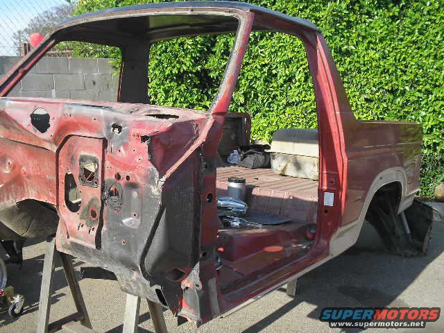 Red Ford Bronco body on stands, stripped down, showing interior and rear quarter panel