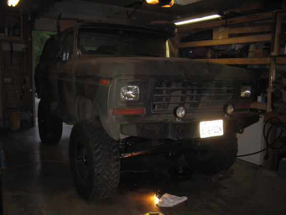 Camouflaged Ford Bronco with lifted suspension and off-road tires parked in a garage