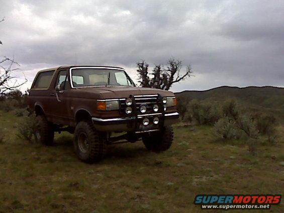 1990 Ford Bronco parked in a grassy field with scrub brush and hills in the background