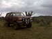 1990 Ford Bronco - Brown 1990 Ford Bronco with aftermarket lights and large tires sits in a rural landscape.