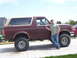 1990 Ford Bronco - A man poses with a lifted Ford Bronco, modified with large off-road tires.