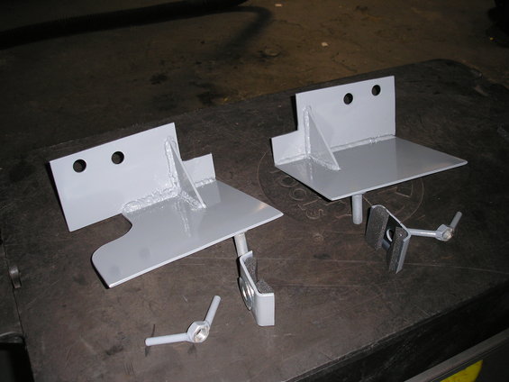 Two grey metal hi lift mount brackets with hardware on a dark surface