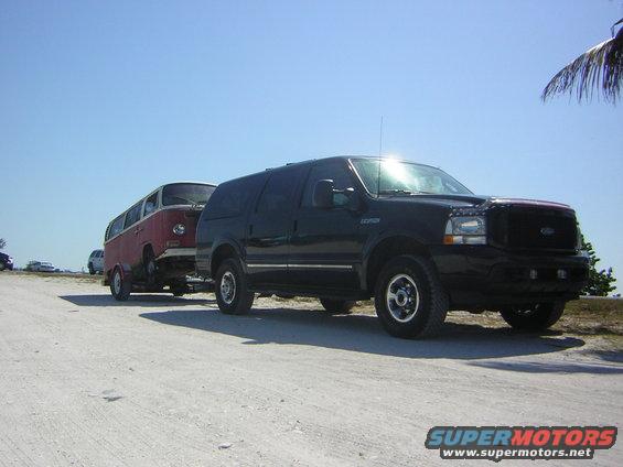 1971 Volkswagen bus being towed by a black Ford Excursion on a dirt road