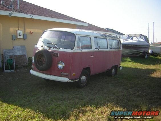 Red and white Volkswagen Type 2 van with spare tire on front, parked on grass