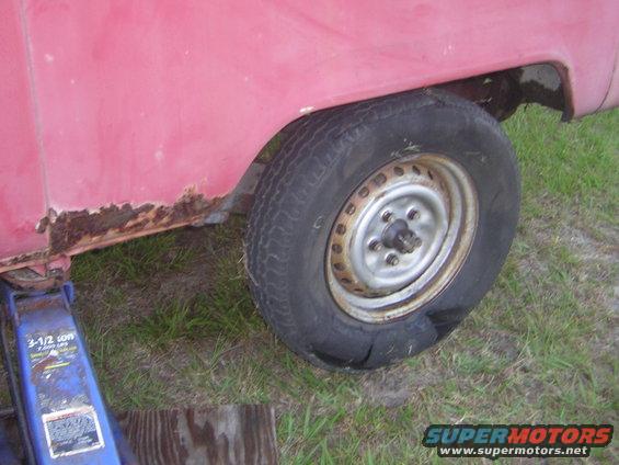 Red van rear wheel well with rust and flat tire on a jack