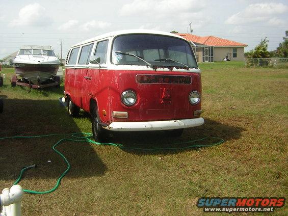 1971 Volkswagen bus, red with white roof, parked on grass with a boat on a trailer in the background