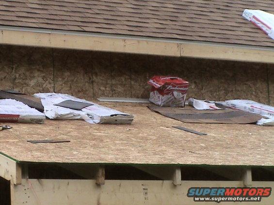 Roof under construction with bundles of shingles and a box of Budweiser