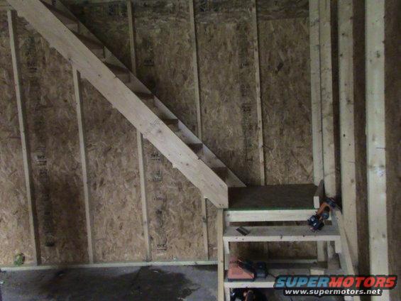 Unfinished wooden staircase and shelving unit in a room with OSB walls