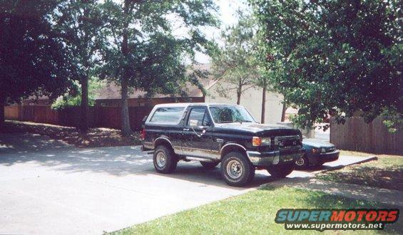 Black Ford Bronco parked in a driveway next to a dark sedan