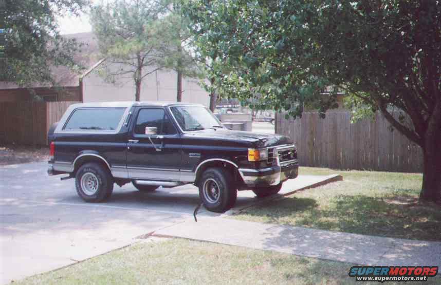 Black Ford Bronco parked on pavement next to grass and a wooden fence