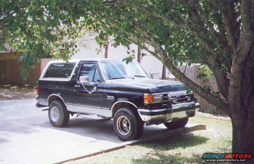 Black and silver Ford Bronco parked under a tree, front quarter view