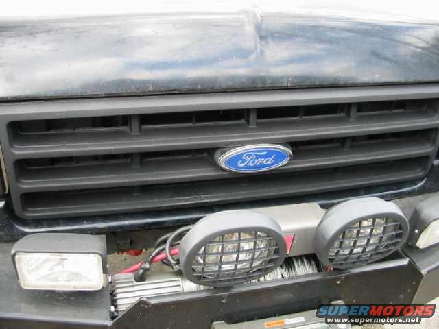 Black 1990 Ford Bronco grille with blue Ford oval badge, two round fog lights, and a rectangular headlight