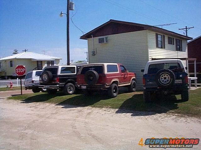 Red Ford Bronco with spare tire on rear door, parked next to other SUVs