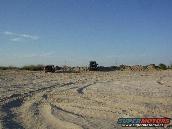 two SUVs parked on a sandy area with tire tracks in the foreground
