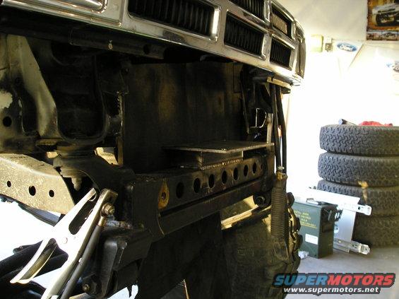 Custom front bumper bracketry with holes, attached to vehicle frame. Tires and ammo can in background