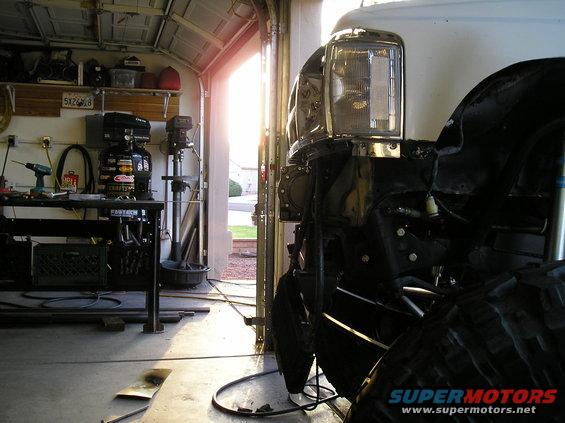 Truck front end with chrome headlight trim and large tire, in a garage with tools on a workbench