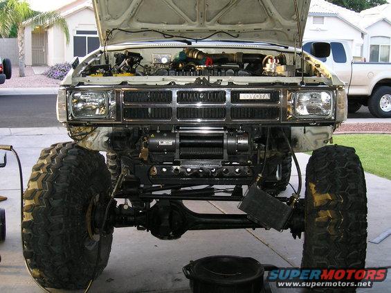 Front view of a lifted 1986 Toyota Hilux with a winch installed on the bumper. Another truck is parked behind it