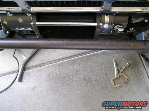 Winch mounted on a vehicle's front bumper. Locking pliers are on the ground