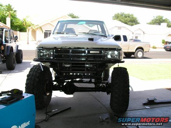 White Toyota pickup truck, lifted with large off-road tires and a front winch, viewed from the front