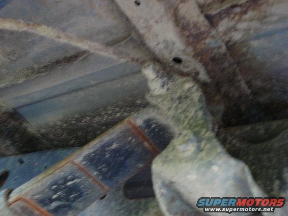 Underside of a rusty vehicle frame with a large metal component covered in grime and moss