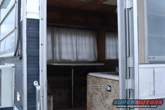 Interior view of a camper, showing curtains, a table, and cabinetry