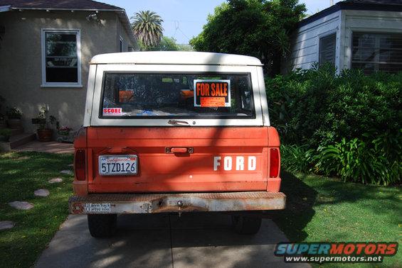 Rear of orange Ford Bronco with white top, 'FOR SALE' sign in window, California plates
