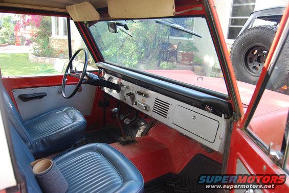 Interior of a red Ford Bronco with blue seats, dashboard, and steering wheel. Spare tire visible outside