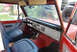 1977 Ford Bronco - The interior of a classic red Ford Bronco shows its dashboard, seats, and steering wheel, with a spare tire visible through the window.