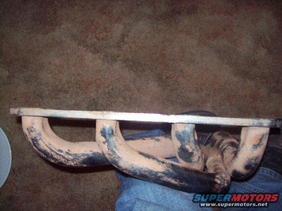 Exhaust manifold with four pipes on each side, resting on a blue surface