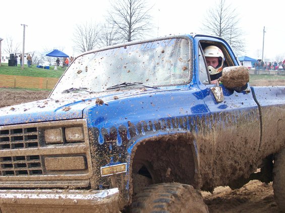 Blue pickup truck covered in mud, driver wearing helmet