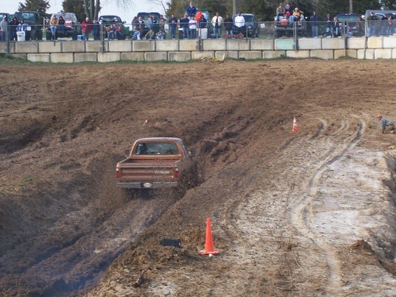 Brown pickup truck stuck in mud, rear view. Appears to be from the 1980s