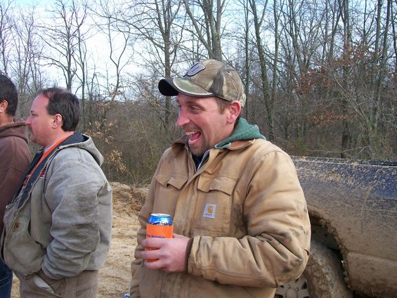 Mud-splattered truck side with a man in a tan Carhartt jacket holding a beer can