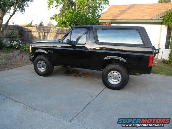 Black Ford Bronco parked on concrete driveway, side view. Appears to be from the 1987-1991 generation