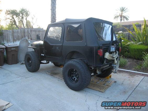 Black Jeep CJ7 with soft top, lifted suspension, and off-road tires parked on concrete