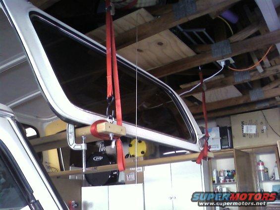 Removable hardtop being lifted by red straps and wooden supports in a garage