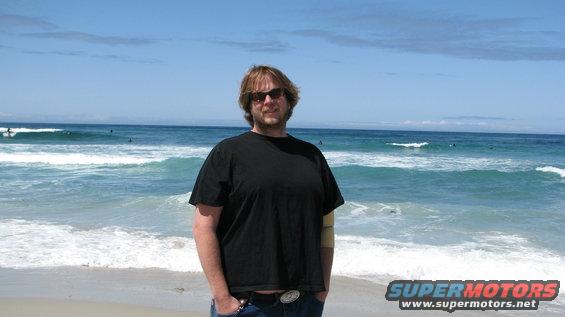 Man in black t-shirt and jeans on a beach with ocean waves and surfers
