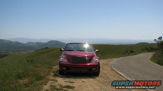 Red 2005 Chrysler PT Cruiser parked on a dirt road with rolling hills and a clear blue sky