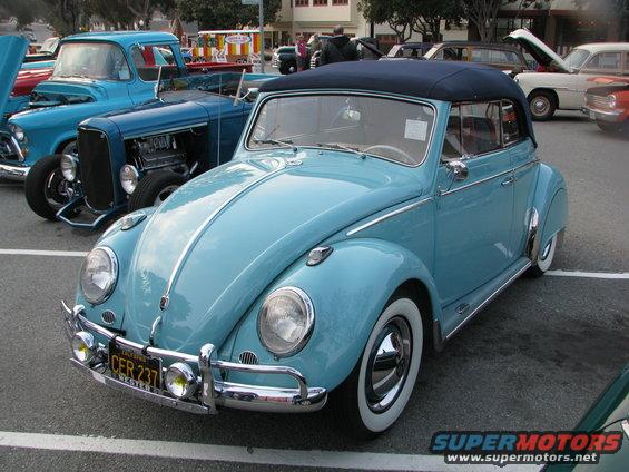 Light blue Volkswagen Beetle convertible parked next to a blue hot rod truck and other cars