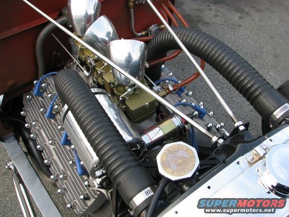 Close-up of a V8 engine with dual carburetors and chrome air cleaners. Black hoses run to the engine
