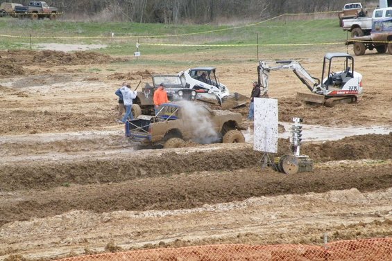 Mud bogging event with a modified truck stuck in mud, a Bobcat loader, and an excavator