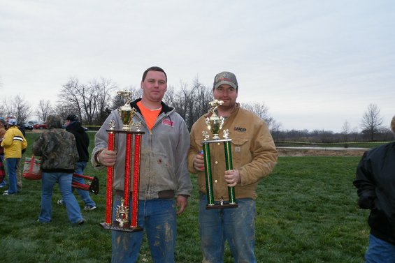 Two men holding large trophies in a grassy field