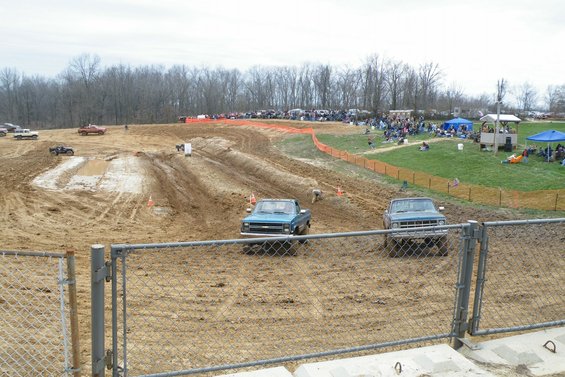 Two pickup trucks on a muddy track with spectators in the background