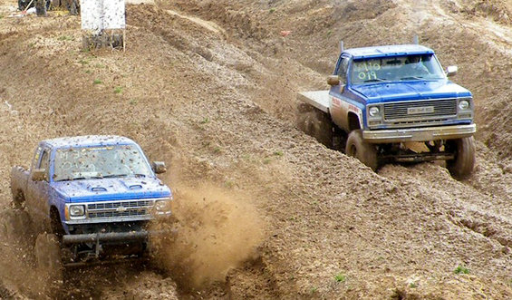 Blue pickup trucks navigating a muddy race course