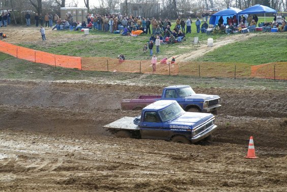 Blue pickup truck with flatbed stuck in mud, another blue pickup truck behind it