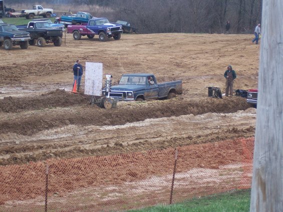 Blue pickup truck stuck in mud pit, people watching