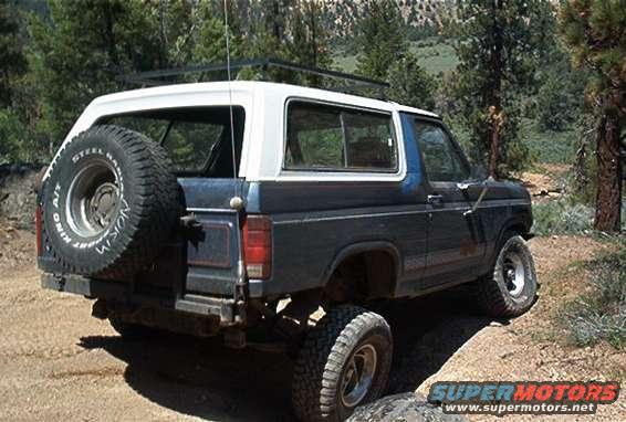 1986 Ford Bronco with spare tire mounted on rear, driving on dirt trail